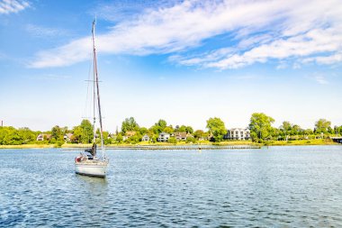 Güneşli bir günün tadını çıkaran bir yelkenlinin resimli görüntüsü sakin bir sahil kasabası yakınlarında
