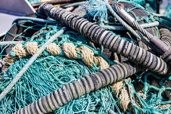 Yıpranmış halat ve şamandıralarla birbirine dolanmış canlı turkuaz balık ağı, deniz yaşamının dokularını ve renklerini gözler önüne seriyor.