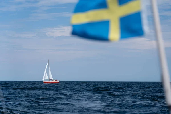 Sailboat on blue open sea with Sweden flag foreground. Concept of travel, adventure and vacation