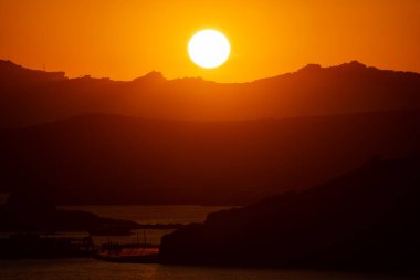 Güneş, deniz önü ile dağ zirvesinin arkasına düşüyor. Muhteşem bir altın gün batımı. Yüksek kalite fotoğraf