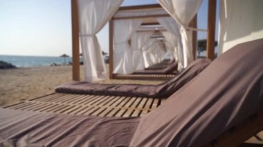 Güneş sandalyesi ve kumsalda beyaz perdeleri olan lüks bir salon. Tatil, rahatlama ve tatil konsepti. Yüksek kaliteli FullHD görüntüler