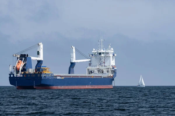 Huge cargo ship and tiny sailboat in the open sea. Concept of difference, diversity and distinction.