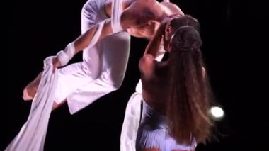 Siyah arka planda beyaz kostümlü hava ipek ikilisi performans sergiliyor. Arzu, çekim ve ilişki kavramı.