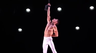 Erkek, kaslı sirk sanatçısı, hava kayışlarıyla arka planda jimnastik numarası yapıyor. Yüksek kaliteli FullHD görüntüler
