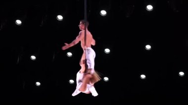 Siyah arka planda beyaz kostümlü hava kayışları ağır çekimde performans sergiliyor. Arzu, çekim ve ilişki kavramı.
