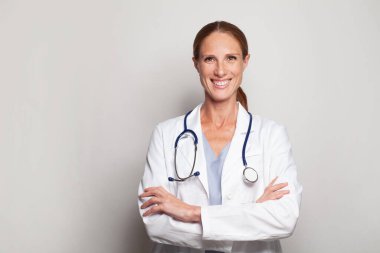 Kolları gri arka planda çaprazlanmış laboratuvar önlüklü çekici bayan doktor.