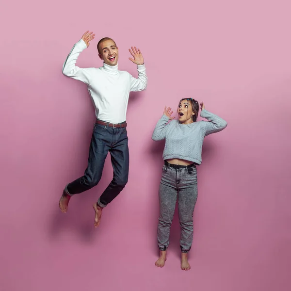 Young jumping people. Young man and woman on bright pink background