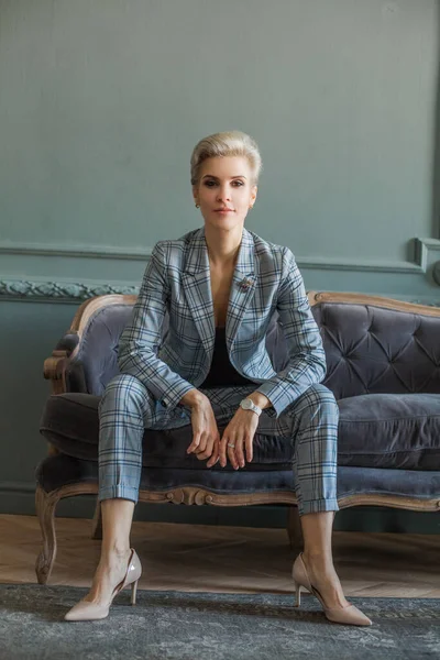 Successful pretty blonde short haired woman in blue suit sitting on the blue sofa