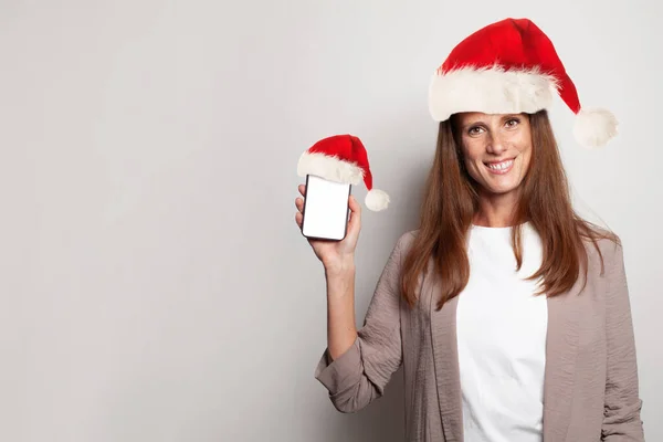 Krásná Brunetka Žena Vánočním Klobouku Drží Mobilní Telefon Prázdnou Obrazovkou — Stock fotografie