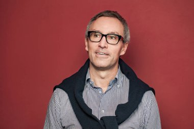 Ciddi bir iş adamı portresi. Kırmızı stüdyo arka planında beyaz saçlı, işaretli gömlek ve gözlüklü.