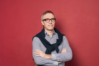 Mavili ve beyazlı olgun işadamı kırmızı stüdyo arka planında gömlek ve gözlükleri kontrol etti.