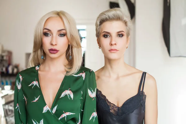 Two beautiful blonde women in nice gowns are standing together
