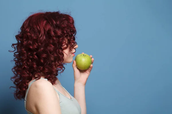 グラマラスな女性とともに赤巻き毛でグレートップ立ち横とホールドグリーンアップルオンブルースタジオ壁の背景 — ストック写真