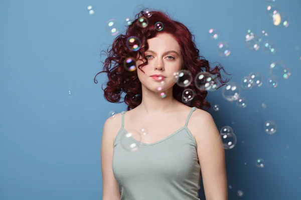 Krásná Žena Červenými Kudrnaté Vlasy Mýdlové Bubliny Modrém Pozadí Studio — Stock fotografie