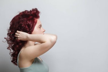Beautiful woman touching her red curly hair against white studio wall background
