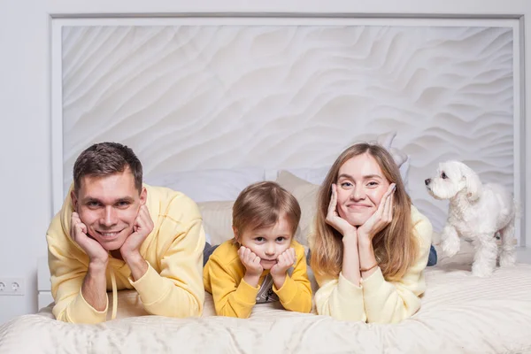 素敵な家族の肖像画 優しい両親 お母さんとお父さんかわいい子供の息子とベッドの上の白い犬 — ストック写真