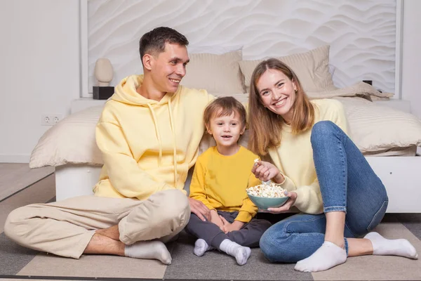 stock image Laughing smiling parents with child son sitting by the bed and eating popcorn
