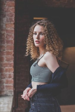 Mavi ceketli, kıvırcık saçlı ve kameraya bakan güzel bir kadın.