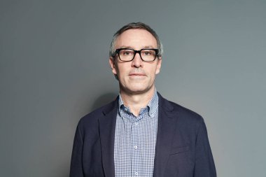 Mavi takım elbiseli olgun bir işadamı, gri duvarda gömlek ve gözlük var.