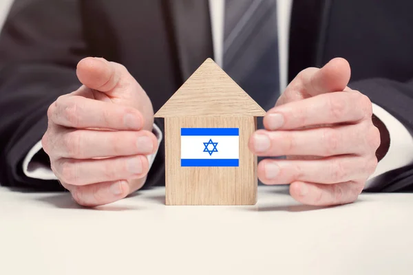 ビジネスマンの手は イスラエルの旗と木製のホームモデルを保持します 保険と財産の概念 — ストック写真