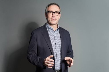 Portrait of mature businessman in suit, checked shirt and glasses is explaining hs business ideas on grey studio background