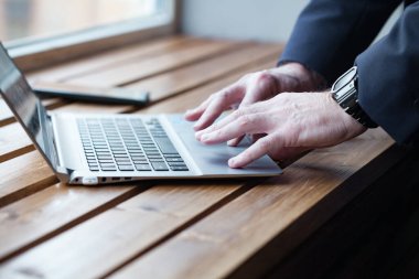 Businessman hands with watch working on laptop, fingers typing on the keyboard. Close up on the wooden table