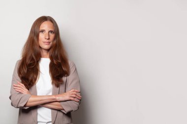 Serious successful business woman standing with crossed arms against grey studio wall background with copy space