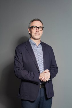 Portrait of mature businessman in suit, shirt and glasses is looking to the camera on grey studio background