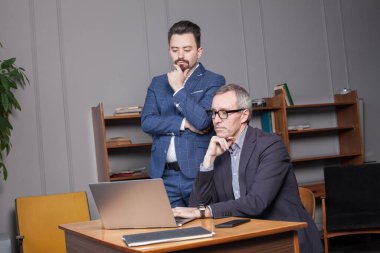 Mavi takım elbiseli ve iş arkadaşıyla gözlüklü dalgın bir iş adamı laptopun başındaki işi düşünüyor.