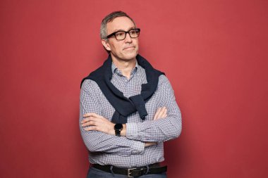 Portrait of serious mature businessman in light blue and white shirt and glasses against red studio background