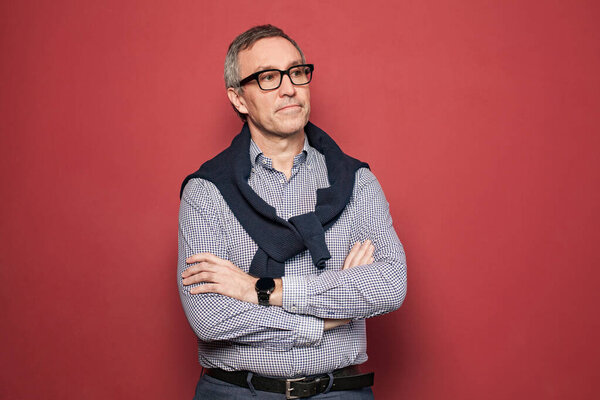 Portrait of serious mature businessman in light blue and white shirt and glasses against red studio background