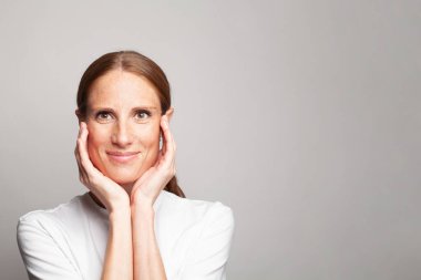 Mükemmel orta yaşlı kadın temiz, sağlıklı tenine dokunuyor elleri beyaz arka planda.