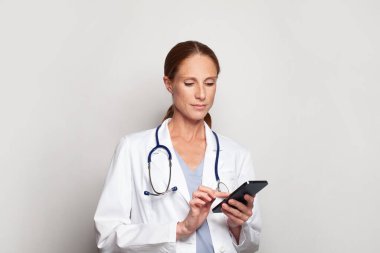 Tıp, teknoloji ve sağlık hizmetleri kavramı. Başarılı bir orta yaşlı kadın doktor doktor ya da elinde akıllı telefon tutan hemşire.