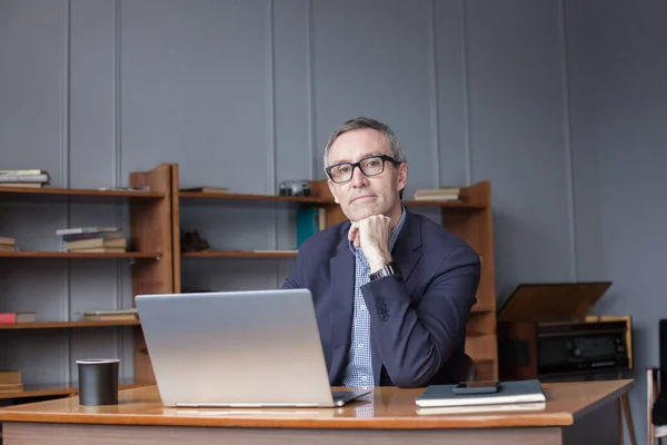 stock image Mature pensive businessman in glasses and suit is thinking about his work by the laptop