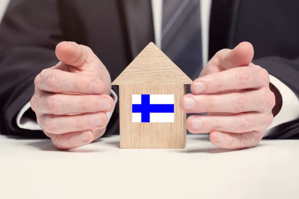 Businessman hand holding wooden home model with Finnish flag. insurance and property concepts
