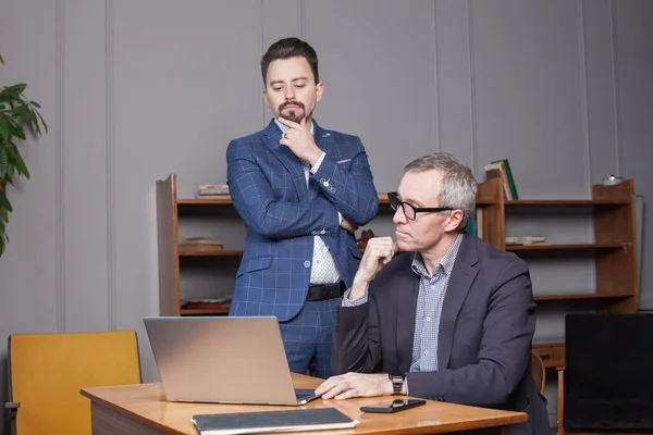 同僚とスーツや眼鏡で成熟したビジネスマンは オフィスのラップトップによる新しい仕事について必死に考えています — ストック写真