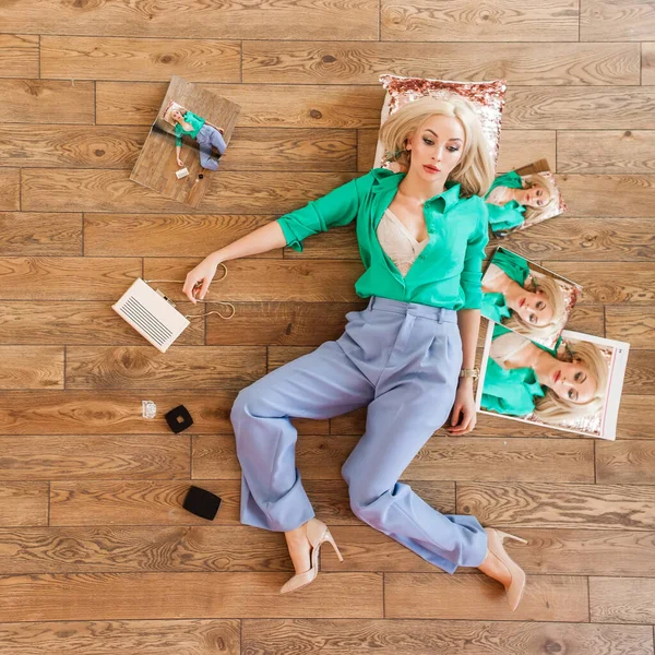 美しいブロンド女性で緑のシャツを着た彼女の周りに化粧品や雑誌と枕の上に木製の床に横たわって — ストック写真