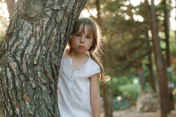 公园里穿着白衣的可爱小女孩站在一棵树旁 — 图库照片