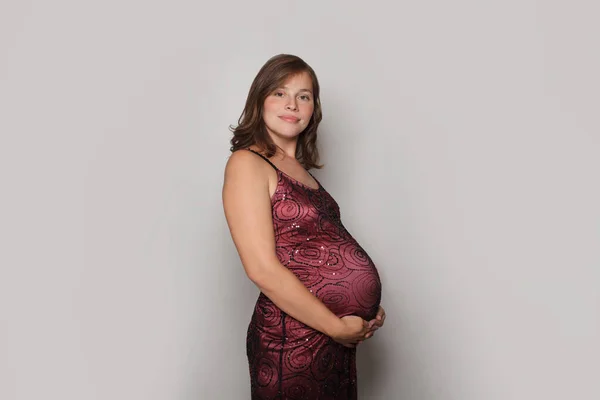 穿着红色衣服的漂亮孕妇站在灰色工作室的墙上 — 图库照片