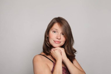 Stüdyoda, kıvırcık saçlı güzel esmer kadın modelin beyaz stüdyo arka planında poz verirken sevimli bir gülümsemeyle kameraya baktığı bir fotoğraf.