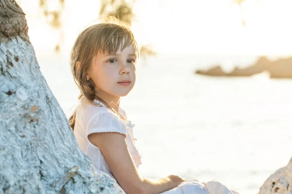 Menina Criança Roupas Brancas Sentado Perto Árvore Fundo Mar Azul — Fotografia de Stock