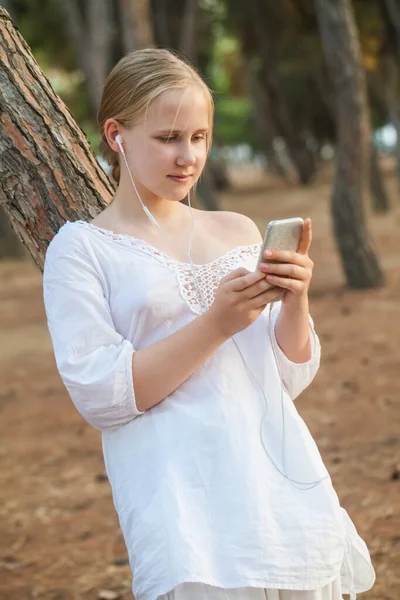 Teenage Dívka Bílém Oblečení Sluchátka Drží Mobilní Telefon Stojí Blízkosti — Stock fotografie