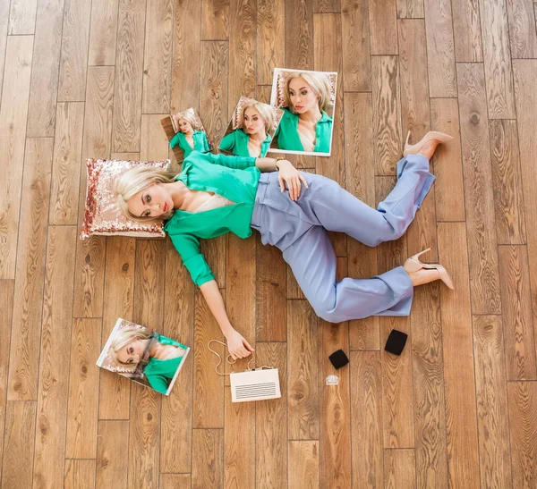 ブロンド女性で緑のシャツを着た彼女の周りの化粧品や雑誌と枕の上に床に横たわっています — ストック写真