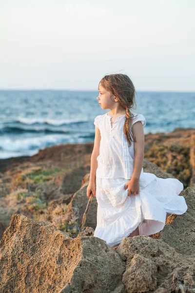 青い海を背景に岩の上に立つ白い服の少女 — ストック写真