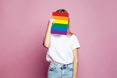 Güzel bir kadın, kimliğini pembe arka planda saklamak için kağıt bir LGBT bayrağı kullanıyor.