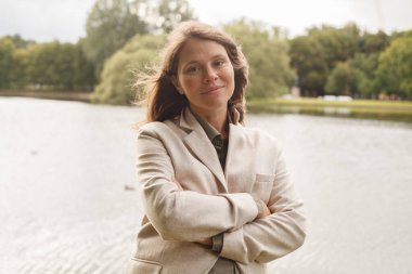 Kahverengi saçlı, sevimli, gülümseyen bir kadın. Dışarıdaki kameraya bakıyor.