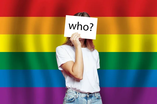 Anonymous LGBT woman covering face with white paper on LGBT flag background. Questioning concept