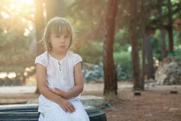 公园里穿着白衣的可爱的黑发小女孩坐在轮胎上 — 图库照片