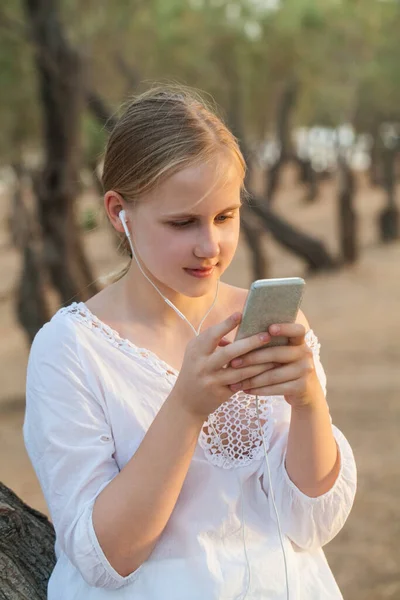 Tonårstjej Hörlurar Håller Mobiltelefon Bakgrunden Skogen — Stockfoto