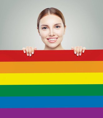 Gri arka planda LGBT bayrağı gösteren neşeli genç kadın.